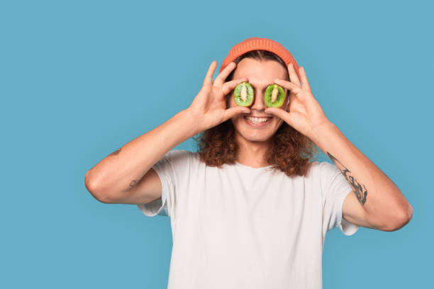 young adult guy covered eyes with kiwi fruit - facial expression isolated lifestyles exoticism imagens e fotografias de stock