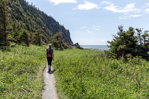 Woman wearing a backpack and hiking on a trail along the St-Lawrence River, Quebec, Canada. This photography was taken at the Bic National Park.