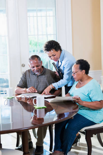 Senior couple at home with financial advisor A senior African-American couple in their 60s sitting at home at their dining room table, looking at documents and talking with a financial advisor. The advisor is a mature African-American woman in her 50s. florida real estate house home interior stock pictures, royalty-free photos & images