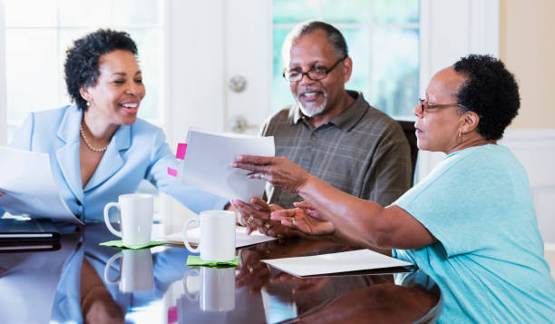 Senior couple at home with financial advisor A senior African-American couple in their 60s sitting at home at their dining room table, looking at documents and talking with a financial advisor. The advisor is a mature African-American woman in her 50s. cpa offers stock pictures, royalty-free photos & images
