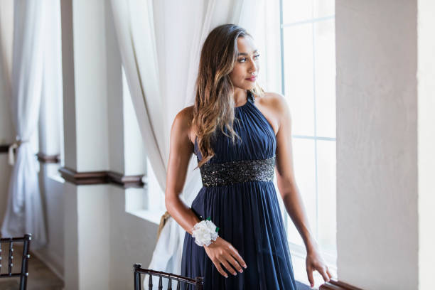 Mixed race teenage girl wearing prom dress A mixed race teenage girl, 16 years old, standing by a window, wearing a prom dress and wrist corsage. prom dress stock pictures, royalty-free photos & images