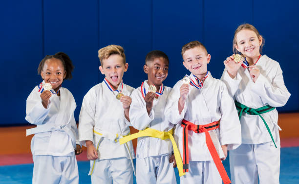 Children showing off their taekwondo medals A multi-ethnic group of five children wearing taekwondo uniforms proudly showing off their medals for winning a competition. The boys are 7 years old. The African-American girl is 6 and the other girl is 9. winners podium photos stock pictures, royalty-free photos & images