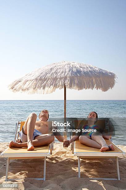 Young Couple On Sun Loungers Holding Hands Stock Photo - Download Image Now - Beach, Lounge Chair, Italy