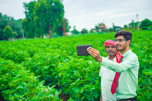 Young indian agronomist taking selfie with farmer at field