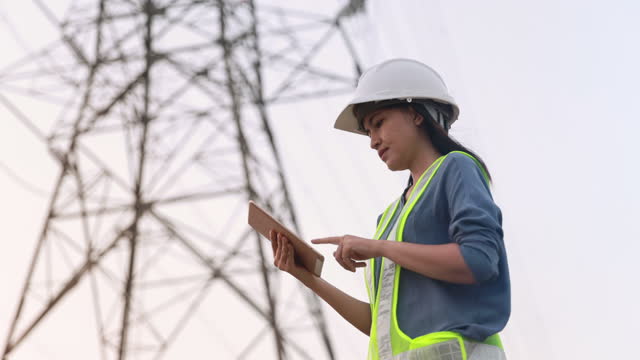 female electrical engineer working on digital tablet with electric power pole background
