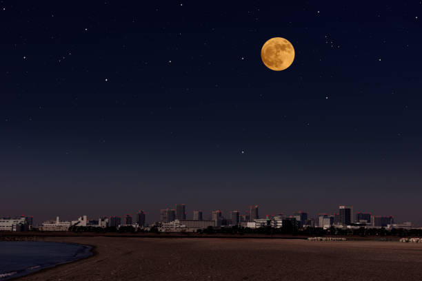 istock Full moon rising over the urban skyline seen from the beach 1301130497