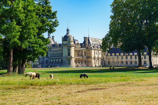 Chantilly, France - September 21 2020: Rear view of Chateau de Chantilly from the English Garden with horses in the foreground - France