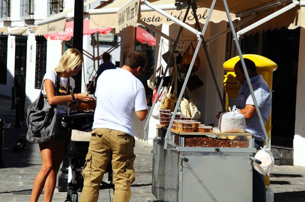 Couple at snack stall, Mijas, Spain. Couple buying honey coated nuts at a road stall in the village centre, Mijas, Spain. mijas pueblo stock pictures, royalty-free photos & images