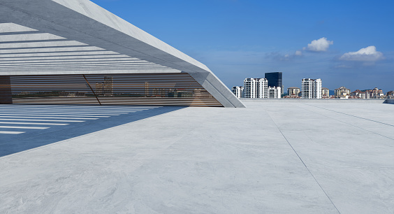 Perspective view of empty concrete floor and modern rooftop building with cityscape. Mixed media