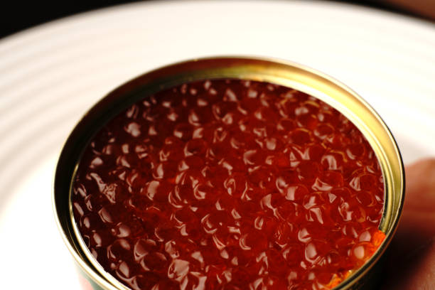 Red caviar in a jar just opened. It's on a white plate. Closeup