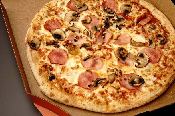 istock Pizza in a box on a black background. With cheese and mushrooms. Top view. 1301147590