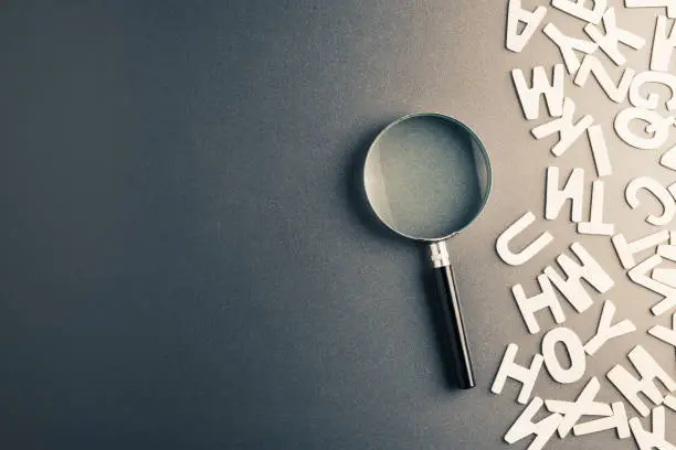 Magnifying glass with part of scattered Engligh alphabt letters on the table
