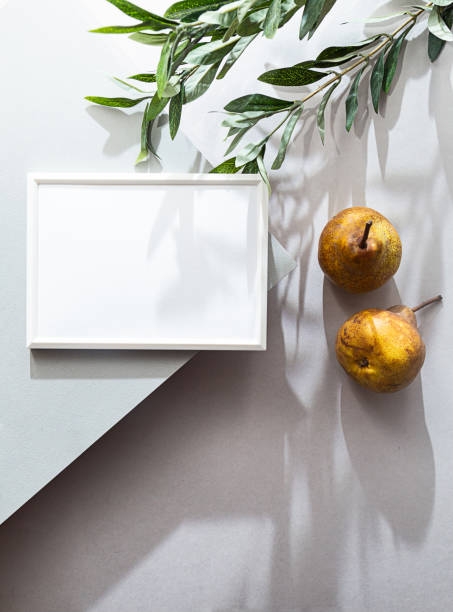 istock Modern still life with white blank photo frame. Summer composition with pears and olive branch shadows. Mockup, flat lay on a light gray background 1301148696