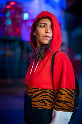 Beautiful urban woman wearing red hooded sweatshirt, standing at street at night in Moscow, looking away, copy space