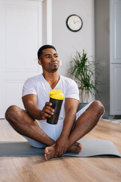 istock African-American man sitting cross-legged and relaxing on exercise mat after workout, drinking water 1301151745