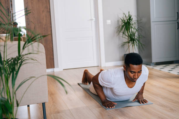 istock African-American man practicing burpee exercise at home, doing push-ups and jumping on yoga mat. 1301151961