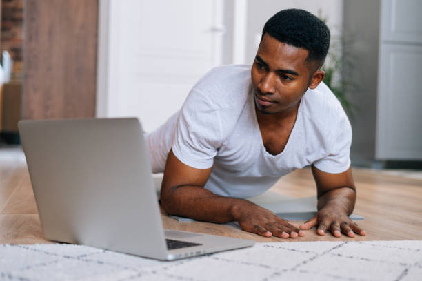 istock Close-up of strong African-American man exercising workout in horizontal plank position using laptop 1301152561