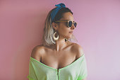 Portrait of a fashionable young girl with big golden earrings, sunglasses on pink background.