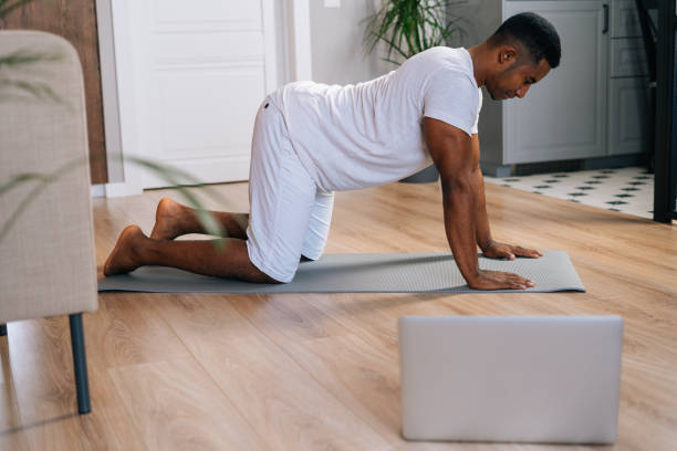 istock African-American man have online training using laptop working out, doing stretching exercise on mat 1301153846