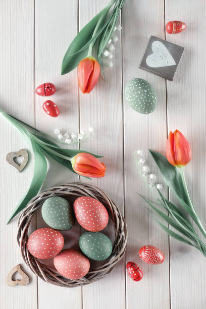istock Flat lay with red tulips in rattan wreath basket and green grass. Decorative painted Easter eggs. Spring or Easter background on rustic off white wooden table. Zero waste sustainable low impact decor 1301157799