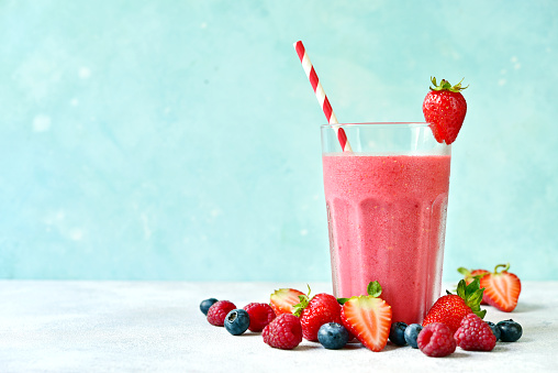 Fresh cold strawberry smoothie in a tall glass on a light blue slate, stone or concrete background.