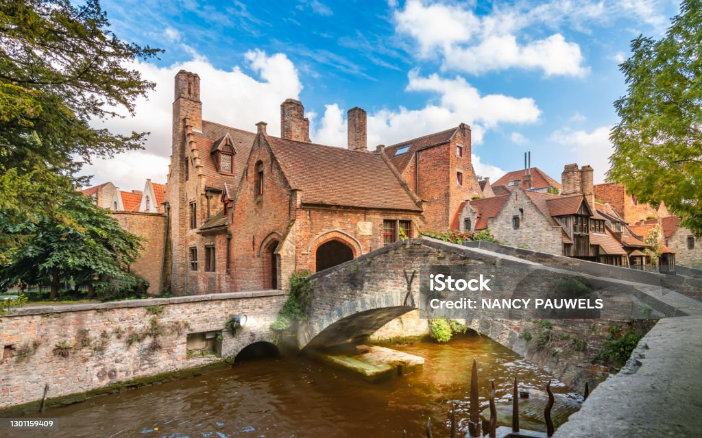 Old famous canal bridge in Bruges Belgium. Popular tourist attraction, romantic old lovers bridge over canal in Bruges. No people. Blue sky, white clouds. Bruges Stock Photo