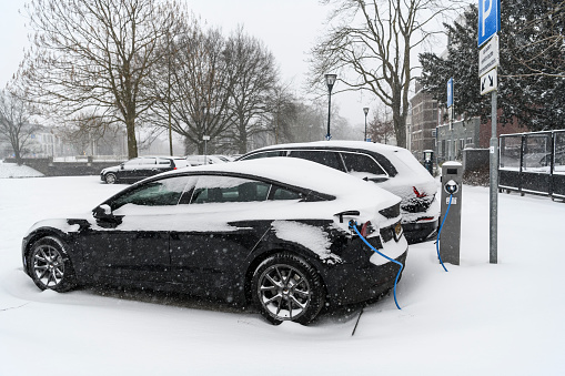 Electric cars charging at an electric vehicle charging station during a cold winter day with fresh snow on the cars in the city center of Zwolle. The Tesla model 3, Audi eTron and Tesla Model S are covered in a layer of snow.