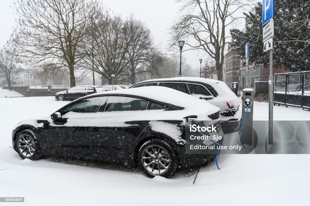 Electric cars charging at an electric vehicle charging station during a cold winter day Electric cars charging at an electric vehicle charging station during a cold winter day with fresh snow on the cars in the city center of Zwolle. The Tesla model 3, Audi eTron and Tesla Model S are covered in a layer of snow. Winter Stock Photo