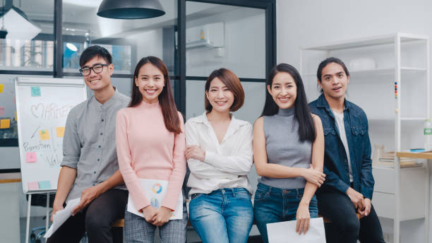 grupo de jóvenes creativos asiáticos con ropa informal inteligente mirando la cámara y sonriendo en el lugar de trabajo creativo de la oficina. - asia fotografías e imágenes de stock