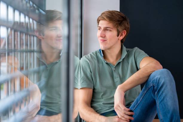 istock Young man sitting by the window and using a mobile phone 1301169709