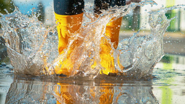 CLOSE UP Unrecognizable girl in yellow rubber boots jumps into the glassy puddle LOW ANGLE, CLOSE UP, DOF: Unrecognizable Female in brand new bright yellow rubber boots jumps into the glassy puddle on the sidewalk. Carefree young woman in rain boots jumps into the big puddle. boot photos stock pictures, royalty-free photos & images