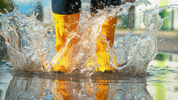 close-up menina irreconhecível em botas de borracha amarela salta para a poça de vidro - human leg women shower water - fotografias e filmes do acervo