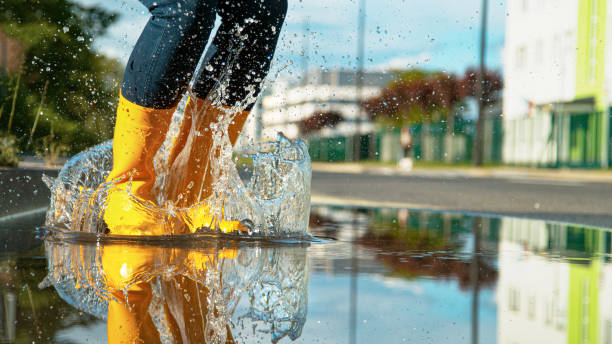 ângulo baixo: garota com botas de borracha amarelas brilhantes pula na poça de vidro. - human leg women shower water - fotografias e filmes do acervo