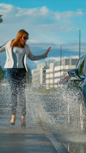 istock VERTICAL: Woman is surprised as she gets splashed with water by careless driver 1301170956