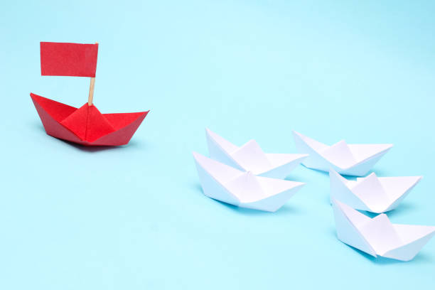 istock Leadership concept, green paper ship leading among white on white background 1301171054