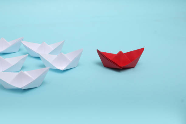 istock Leadership concept. Red leader paper ship leading among white on blue background 1301171103