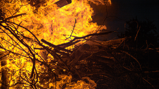 CLOSE UP: Cinematic shot of fiery hot flames engulfing a big pile of dry firewood near a beautiful campsite on a tranquil summer night. Big bonfire gets ignited in the pitch dark of the fall night.