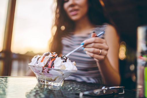 Young Caucasian beautiful woman eating banana split by the river in sidewalk cafe.