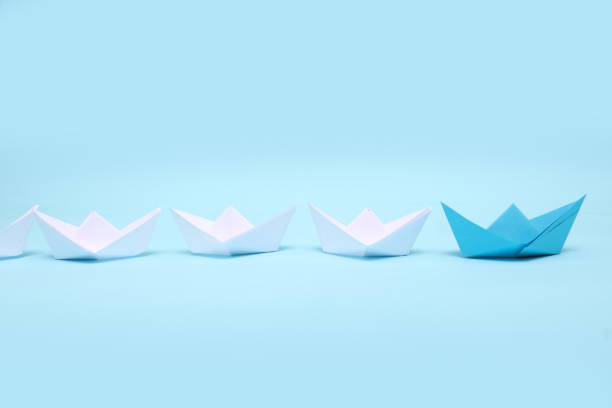 istock Leadership concept. Blue leader paper ship leading among white on Blue background 1301171703