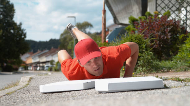 close up: uncoordinated delivery man falls to the ground and drops two pizzas. - uncoordinated imagens e fotografias de stock