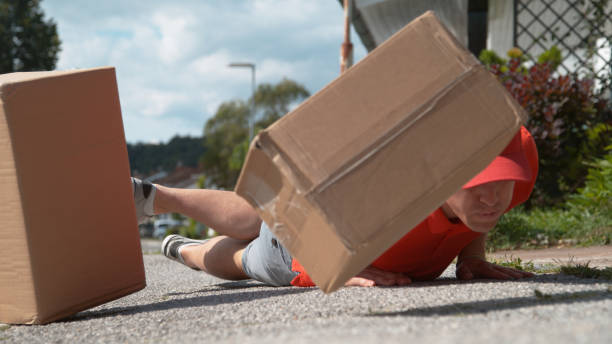 close up: uncoordinated delivery man falls to ground and drops cardboard boxes - uncoordinated imagens e fotografias de stock