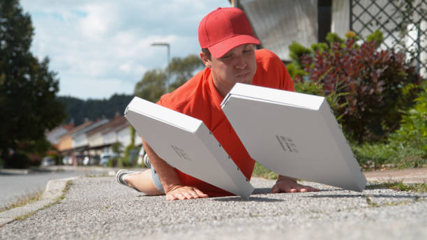 close up: courier trips and falls to asphalt pavement along with two pizza boxes - uncoordinated imagens e fotografias de stock