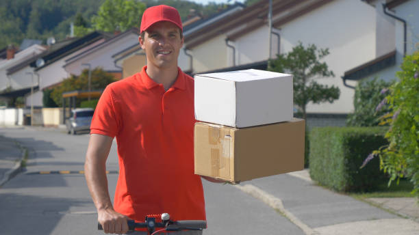 close up: parcel delivery man holds two boxes in one hand while riding escooter. - active seniors enjoyment driveway vitality imagens e fotografias de stock