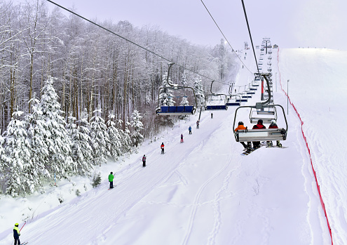 Skiers and snowboarders are lifting on ski-lift. Downhill ride. Adventure skiers season. Skiing and Snowboarding Resorts. Ski and snowboard equipment. Snow sports enthusiasts.