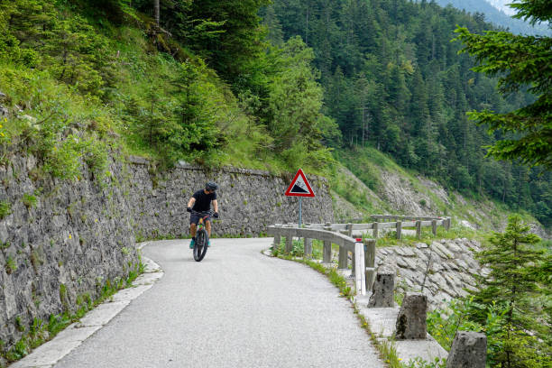 male tourist pedals an electric bike up a steep road in the slovenian mountains. - sport exercising men julian alps imagens e fotografias de stock