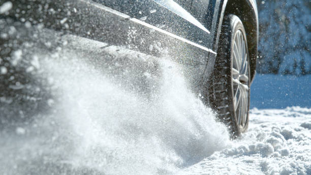 CLOSE UP Low angle shot of vehicle having problems driving along the snowy trail CLOSE UP: Cinematic low angle shot of vehicle having problems driving along the snow covered trail. Glistening small chunks of fresh snow fly in the air as powerful car tries to start on a snowy road. car snow stock pictures, royalty-free photos & images