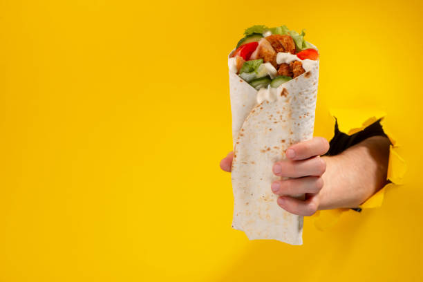 istock Hand giving a doner roll through a torn hole in yellow paper background 1301179897