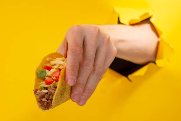 istock Hand giving a taco through a torn hole in yellow paper background 1301180091