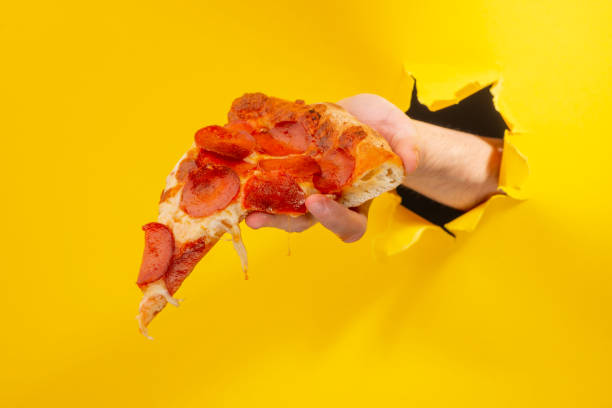 istock Hand giving a pizza slice through a torn hole in yellow paper background 1301180110