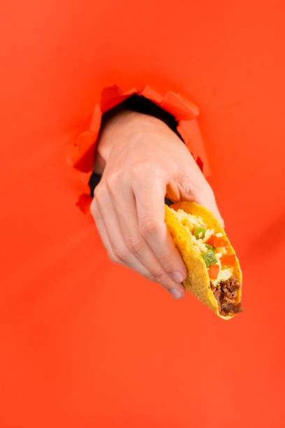 istock Hand offering a taco through a torn hole in red paper background 1301180401